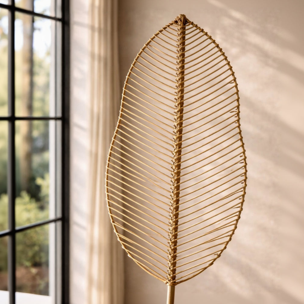 Gold leaf-shaped decorative item against a beige wall with a window in the background
